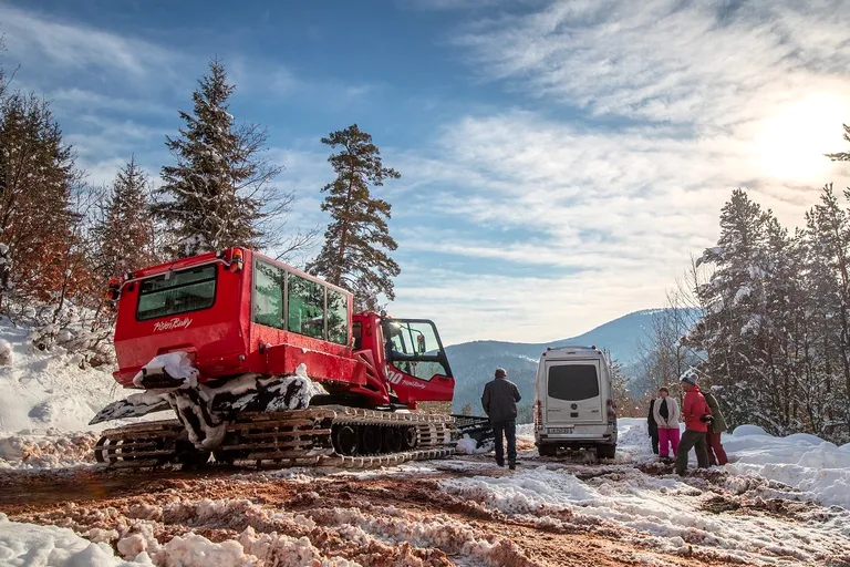 Rode snowcat en een busje aan de rand van het bos, in de zon