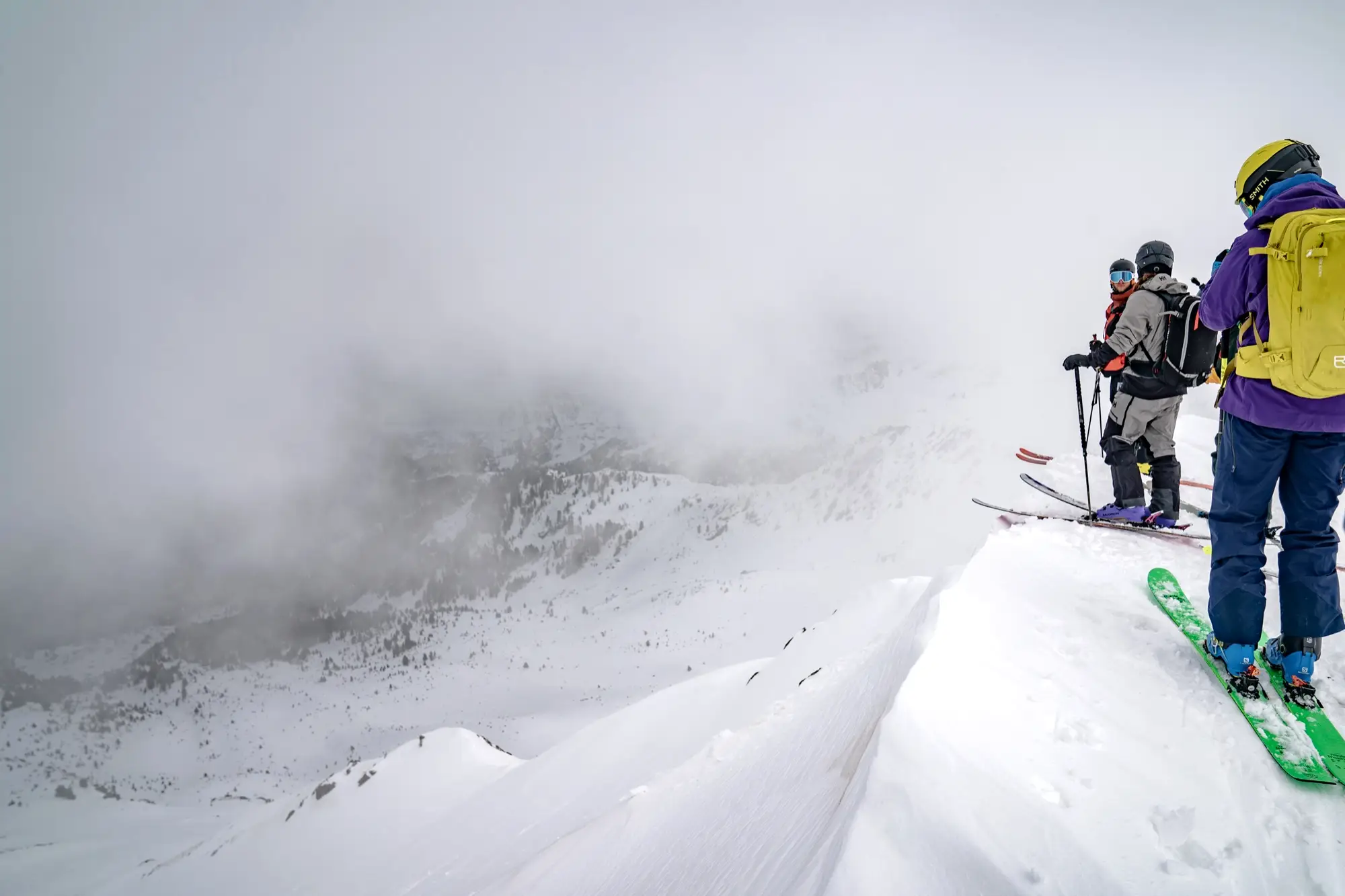 Drie skiërs op een graat in de wolken, klaar om af te dalen