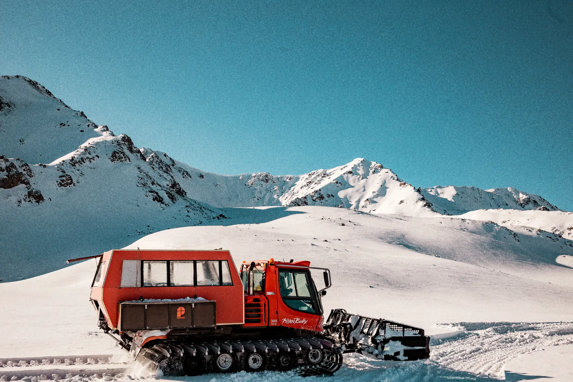 Rode snowcat op een besneeuwde helling met de Tien Sjan erachter