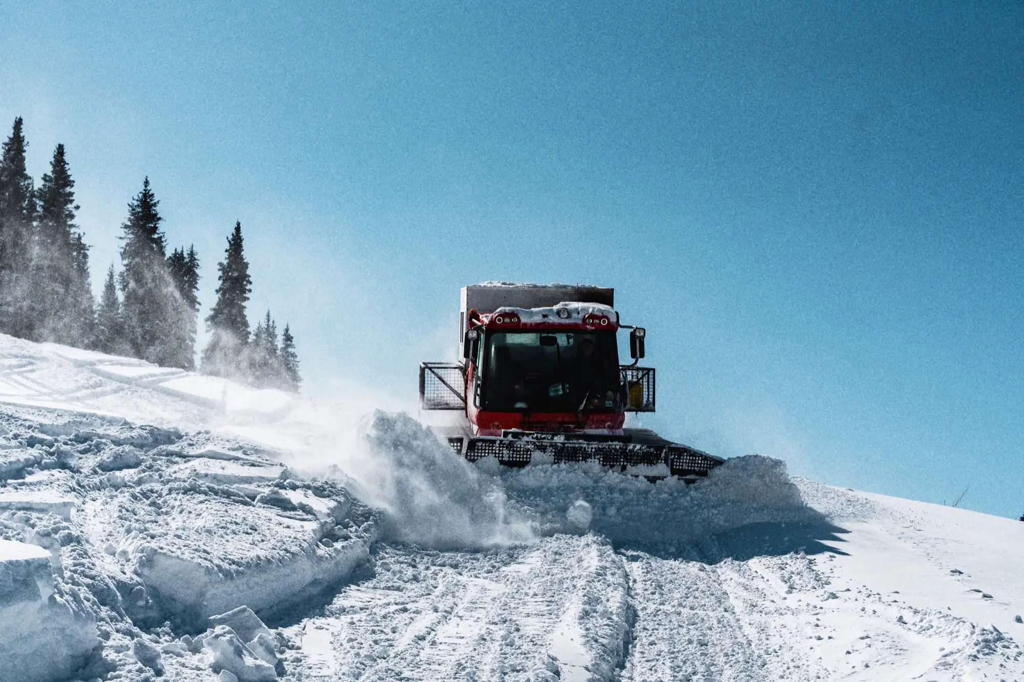 Snowcat ploegt door de sneeuw onder een blauwe lucht