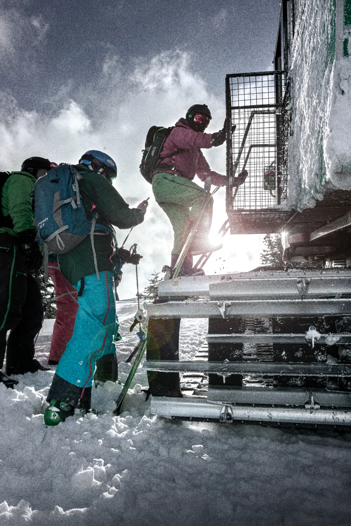 Rijders met ski's en een board klimmen in tegenlicht de cabine van de cat in