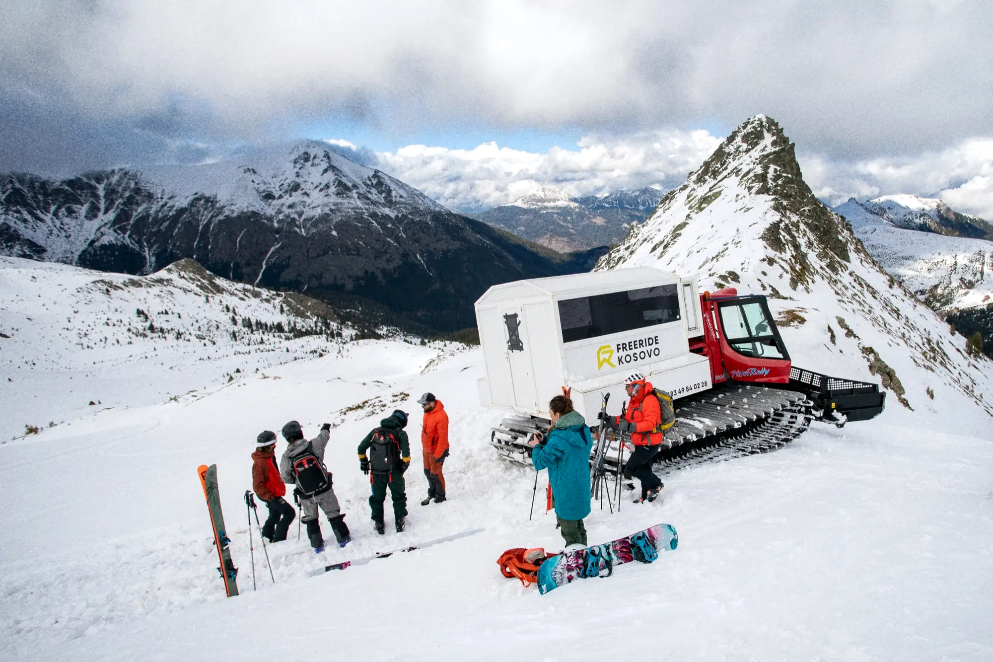 Snowcat met witte cabine en een groep rijders op een besneeuwde rug