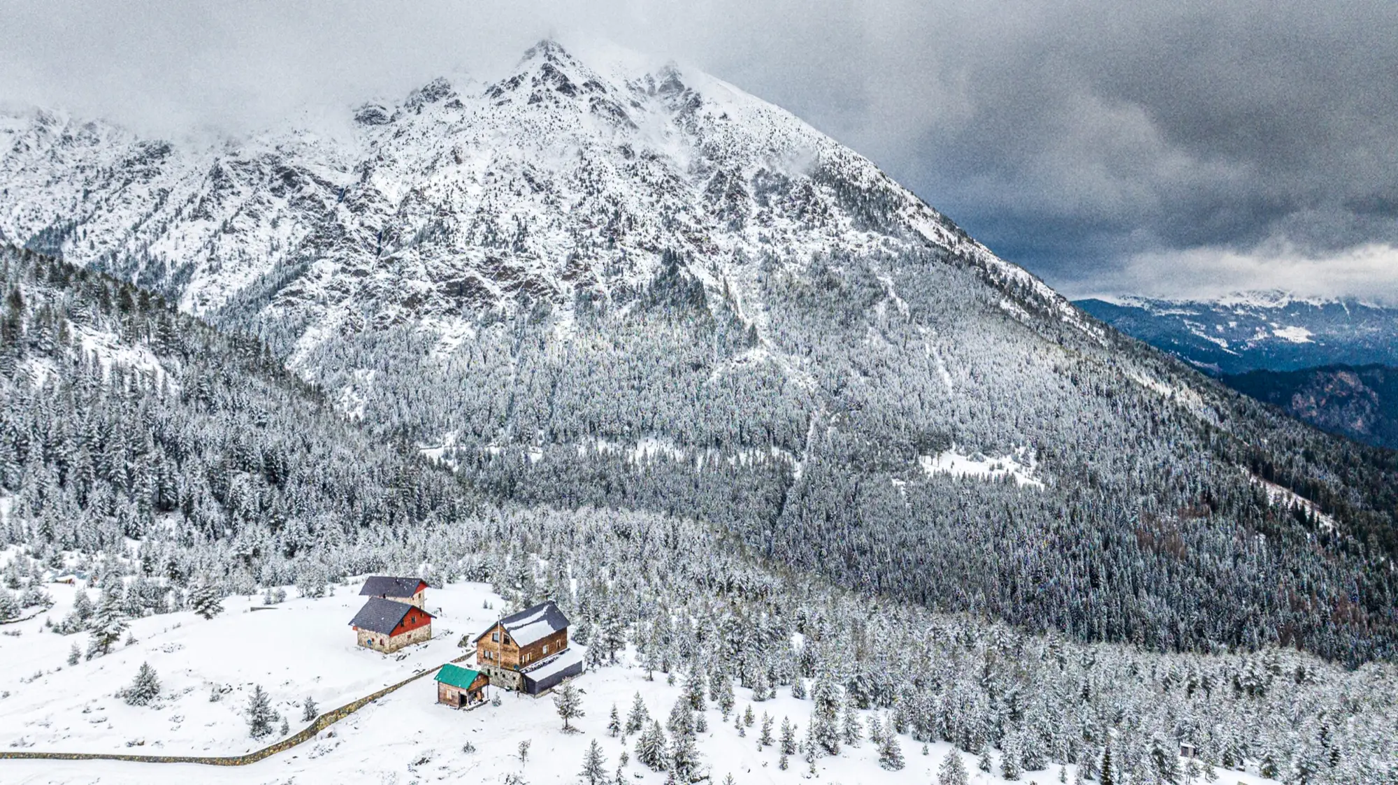 Besneeuwde bergtop boven een bebost dal met een paar houten hutten